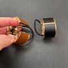 two leather and metal ponytail covers with elastic, shown in black and tan leeather