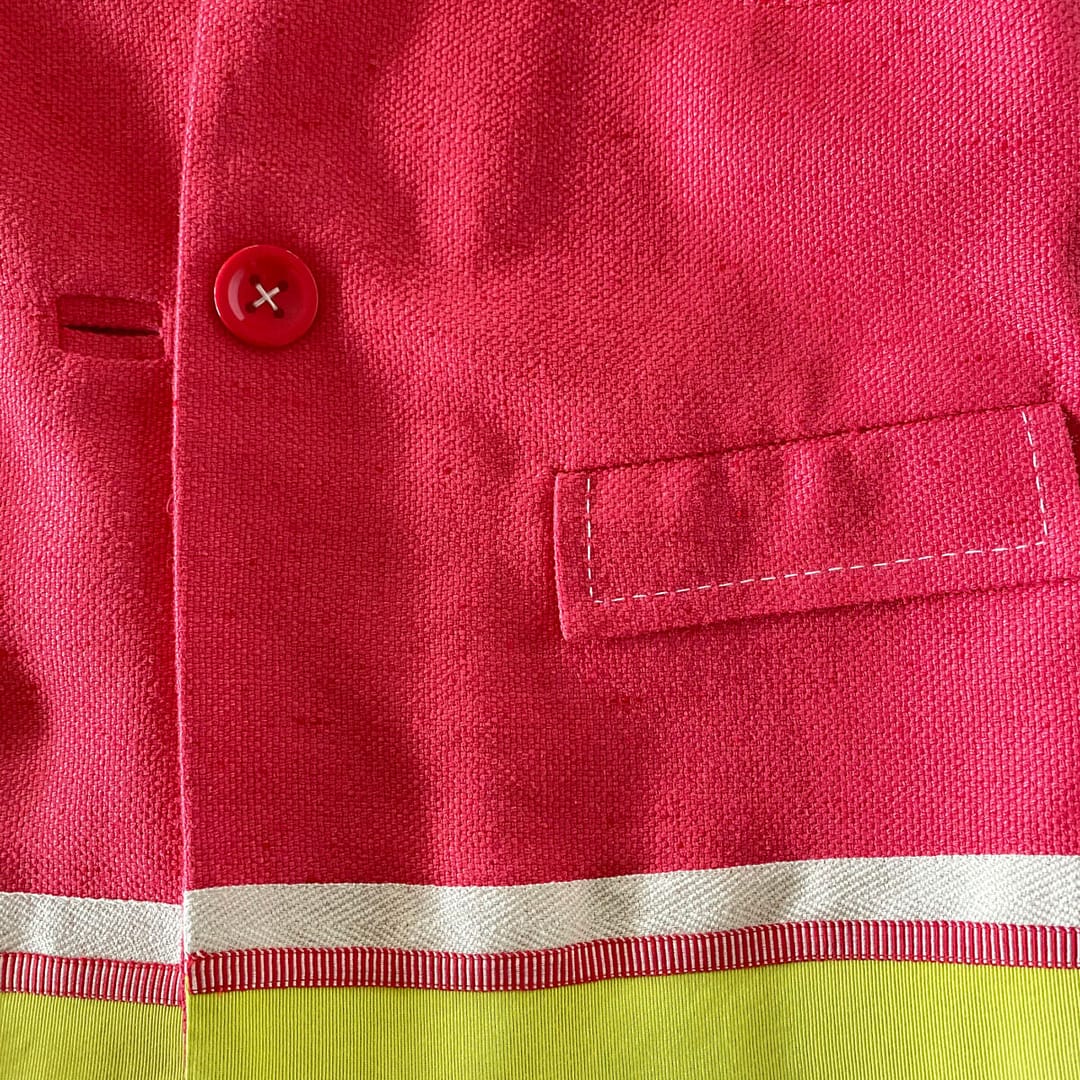 detail of red Rena Lange silk jacket showing button flap pocket and grosgrain ribbon on bottom hem