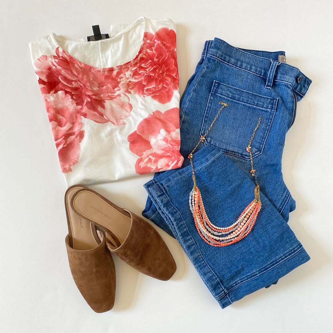A flatlay view of a vintage J.Crew flower tee shirt styled with jeans, a pink necklace and flats