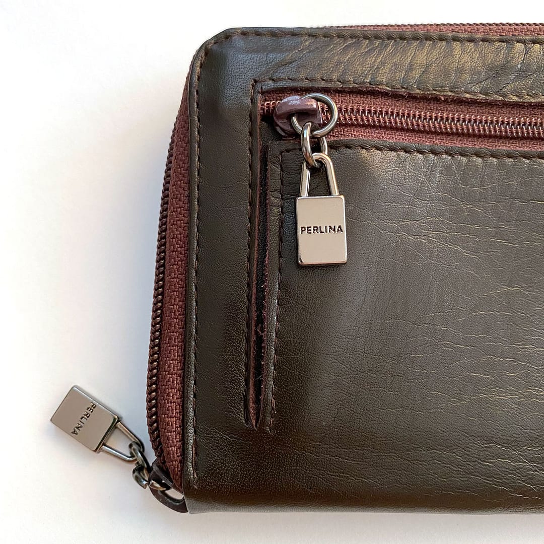 Close up detail of a vintage Perlina large leather wallet showing the back pocket zipper logo pull s well as the logo zipper pull around the entire wallet.