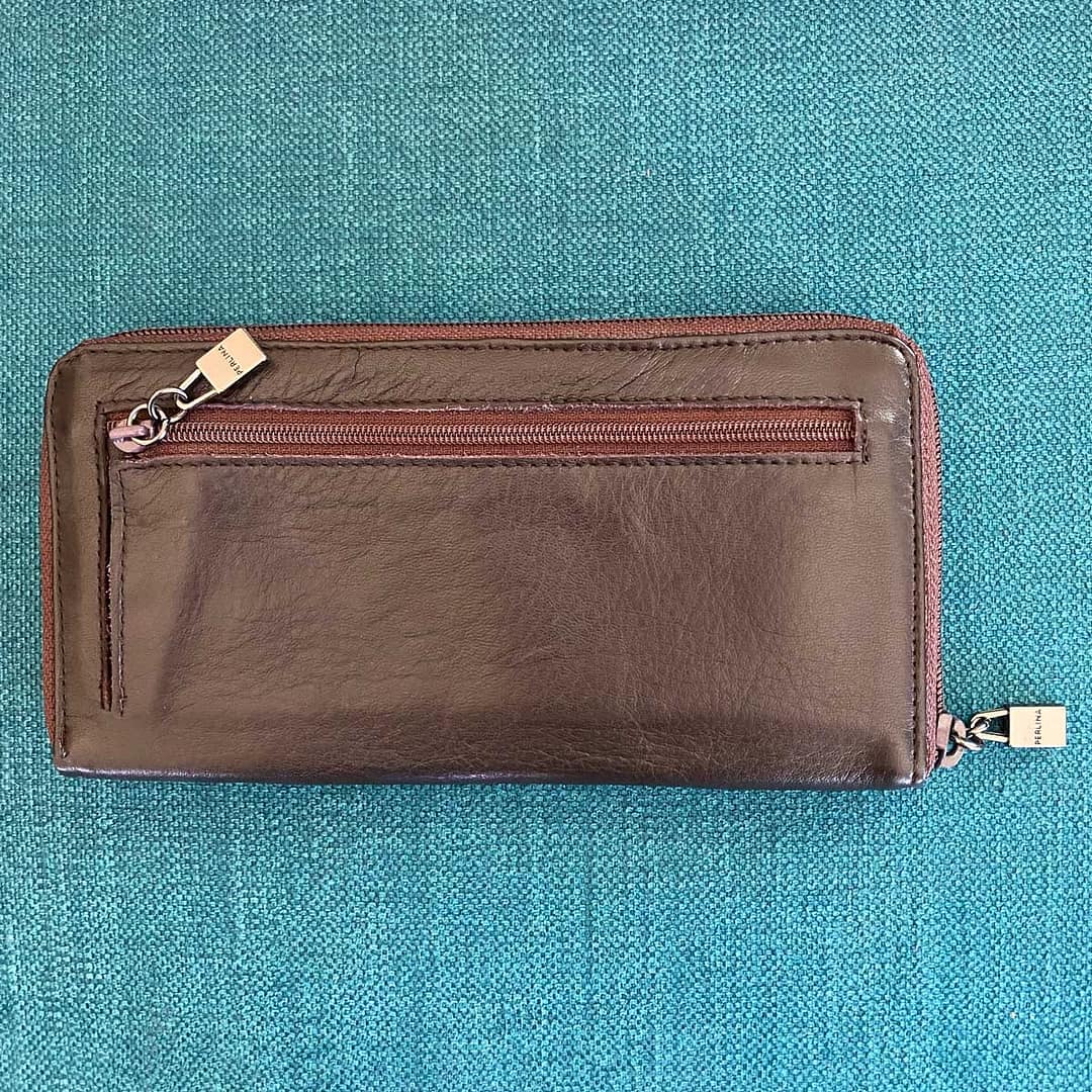 Overhead view of the back side of a vintage Perlina large leather wallet, showing the zipper pocket with logo zipper pull as well as the zipper and logo zipper pull around the entire wallet.