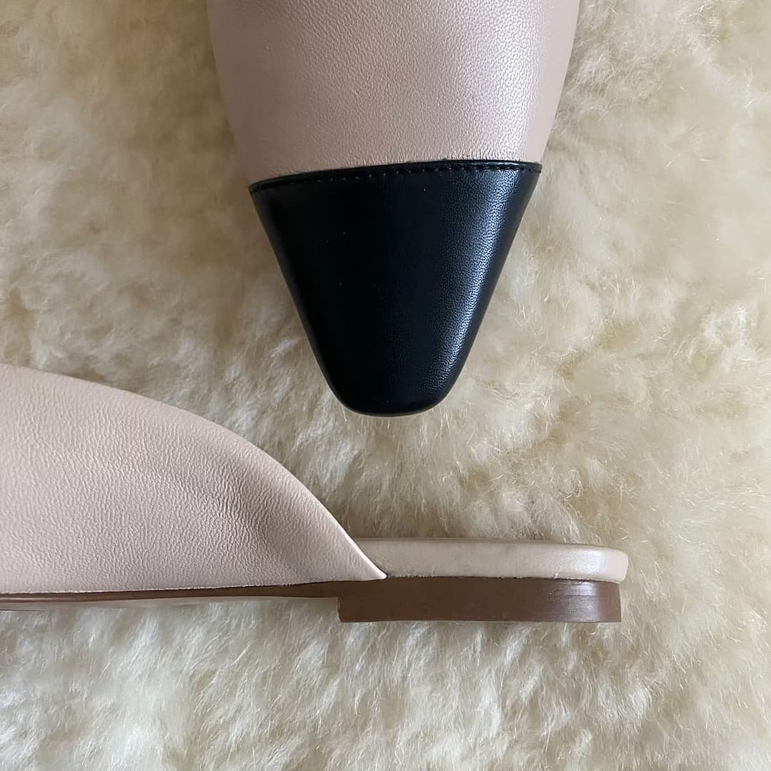 Top view of Banana Republic beige and black ballet mules on a cream background, highlighting the black toe cap and the low, flat heel.