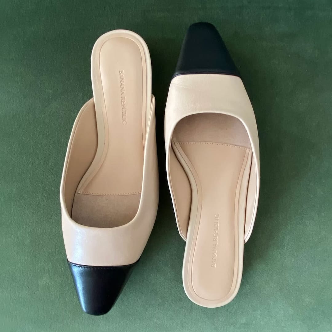 Top view of Banana Republic beige and black ballet mules on a green background, highlighting the backless design and pointed toe.