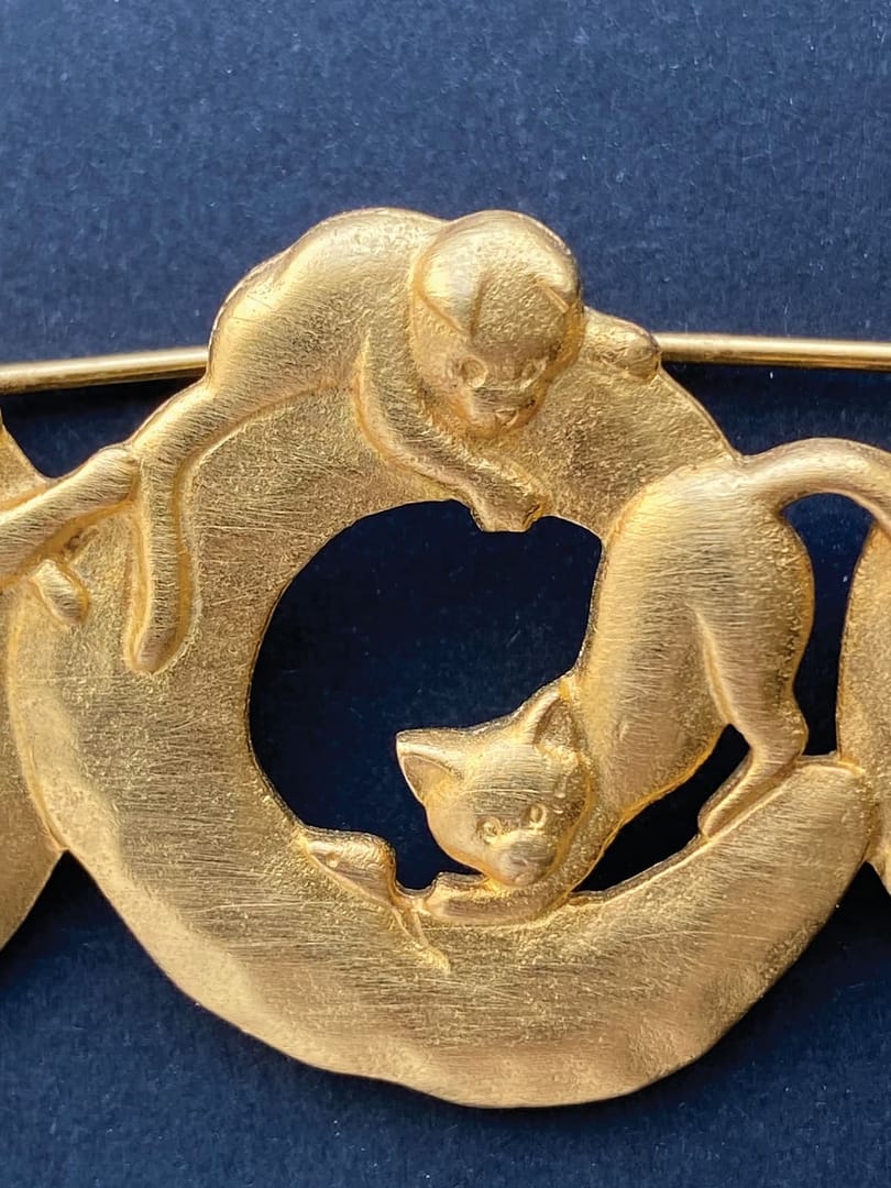Close-up of a signed vintage JJ Jonette gold-tone brooch, featuring two cats interacting on a circular ring.