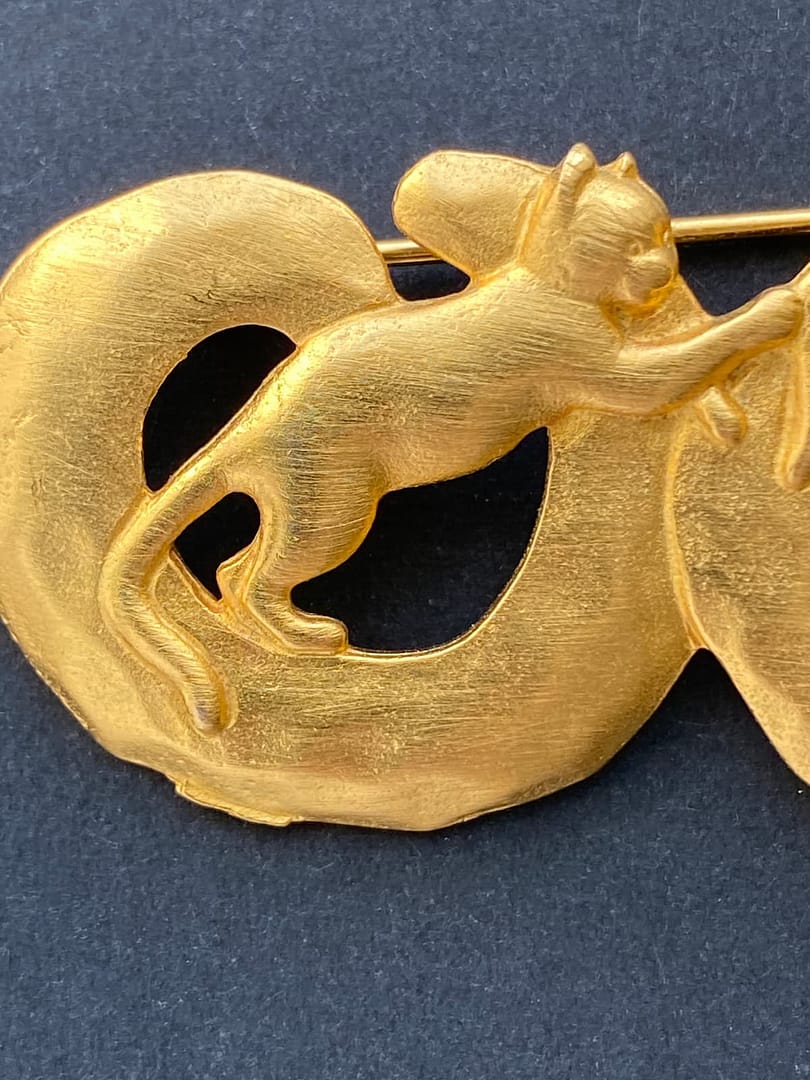 Close-up of a signed vintage JJ Jonette gold-tone cat brooch, showing the textured details of a cat reaching across a circular ring.